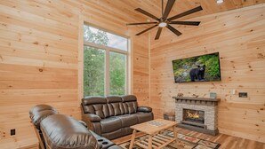 A cozy cabin interior with a leather sofa, a fireplace, and a television mounted on the wall. - 🐻 Bear Crossing🌲 Secluded Views, Hot Tub & Game Room (Gatlinburg)