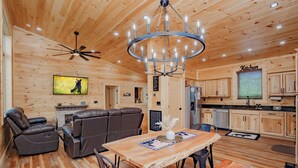 A wooden interior with a dining area, leather sofas, a chandelier, and a kitchen. - 🐻 Bear Crossing🌲 Secluded Views, Hot Tub & Game Room (Gatlinburg)