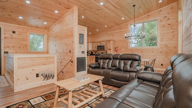 A cozy cabin interior with a wooden interior, a sofa, a dining table, and a kitchen area. - 🐻 Bear Crossing🌲 Secluded Views, Hot Tub & Game Room (Gatlinburg)