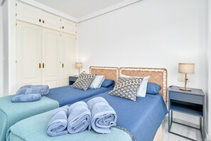Un lit double avec une literie bleue, deux oreillers, une table de chevet avec une lampe et une armoire avec un miroir.
