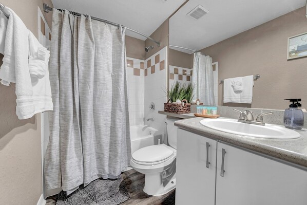 A bathroom with a shower, toilet, sink, and a mirror.