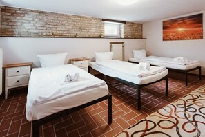 Une chambre d’hôtel avec deux lits simples, un mur en briques, une fenêtre, un radiateur et un tableau.