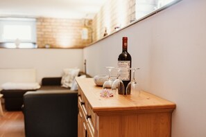 A wooden bar counter with a wine bottle and glasses, a flower, and a couch in the background.