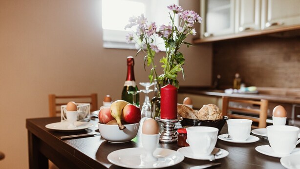 A breakfast setting with a table set for two, including plates, cups, a vase with flowers, and a bottle. - Apartment 'Zuflucht' with Shared Terrace and Wi-Fi (Thale)