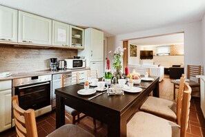 Une cuisine moderne avec des meubles blancs, une table à manger dressée pour quatre personnes et un téléviseur en arrière-plan.