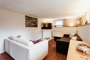 A modern living room with a white sofa, a black sofa, a wooden table, a TV, and a brick wall.