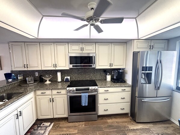 A kitchen with white cabinets, a stainless steel refrigerator, a microwave, an oven, and a ceiling fan.