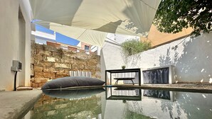 A tranquil outdoor pool area with a stone wall, a bench, and a shaded canopy.