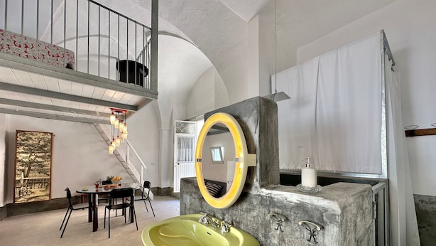 A bathroom with a large, round mirror, a yellow sink, and a stone accent wall.
