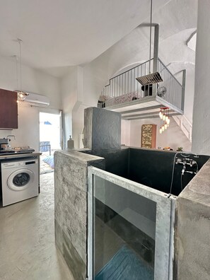 A spacious living area with a high ceiling, a washing machine, and a large black bathtub.