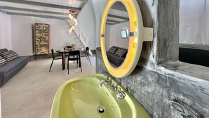 A modern interior with a round mirror, a green sink, a staircase, and a dining area.
