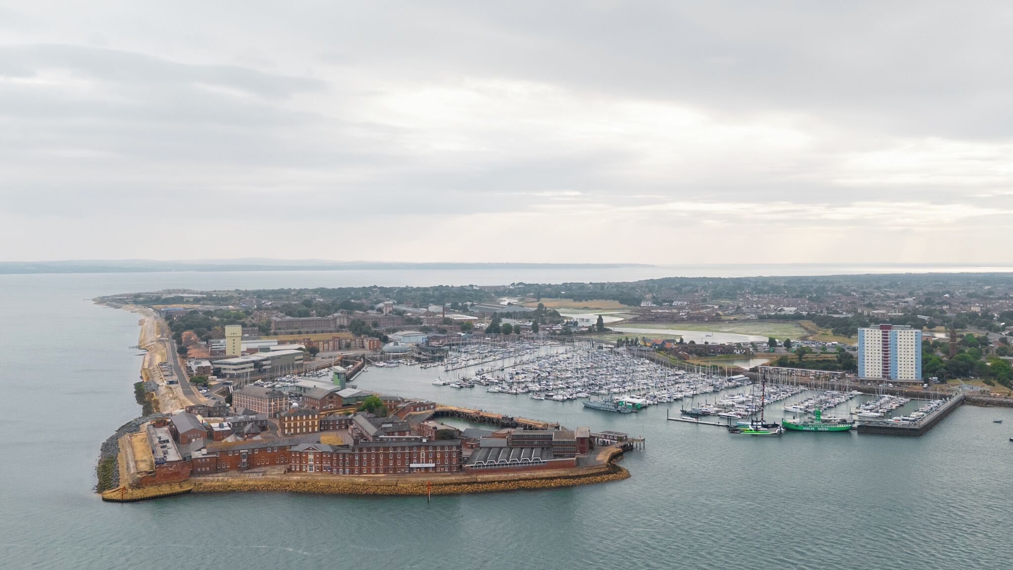 An aerial view of a coastal town with a marina, buildings, and a large body of water.