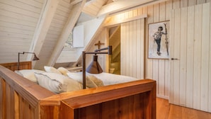 Una camera da letto con soffitto spiovente, travi in legno, un letto con cuscini, una lampada da comodino e un quadro appeso al muro.