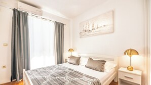 A bedroom with a bed, two bedside tables with lamps, a painting on the wall, and a window with curtains. - A4 apartment with terrace and the sea view, 4 min walk to the beach (Podstrana)