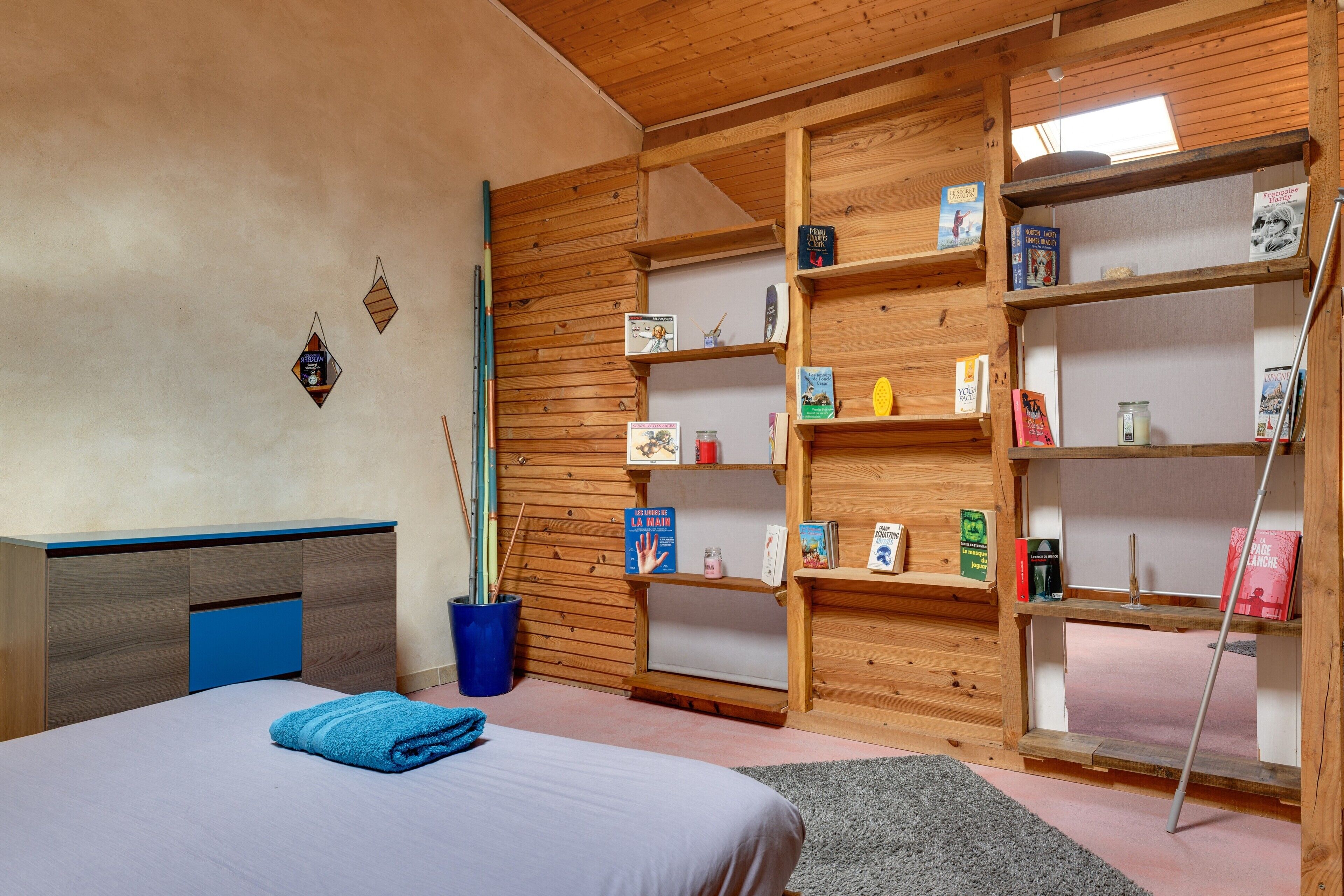 Une chambre à coucher avec un lit, une serviette bleue, une bibliothèque en bois et une fenêtre.