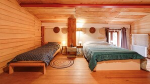 A wooden cabin bedroom with two beds, a wooden floor, a round rug, and a window with curtains. - Le Fil Rouge – A Warm Holiday Home Blending Stone and Design in the Countryside (Saint-Pierre-d'Aurillac)