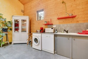 A compact kitchen with a washing machine, microwave, and a small window. - Le Fil Rouge – A Warm Holiday Home Blending Stone and Design in the Countryside (Saint-Pierre-d'Aurillac)
