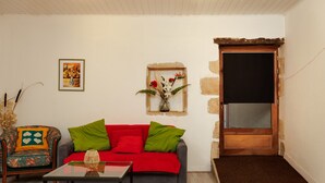A living room with a sofa, a chair, a small table, a framed picture, and a door. - Le Fil Rouge – A Warm Holiday Home Blending Stone and Design in the Countryside (Saint-Pierre-d'Aurillac)