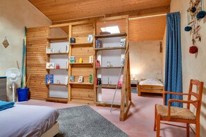 A room with a bed, a chair, a fan, shelves with books, and a blue curtain. - Le Fil Rouge – A Warm Holiday Home Blending Stone and Design in the Countryside (Saint-Pierre-d'Aurillac)