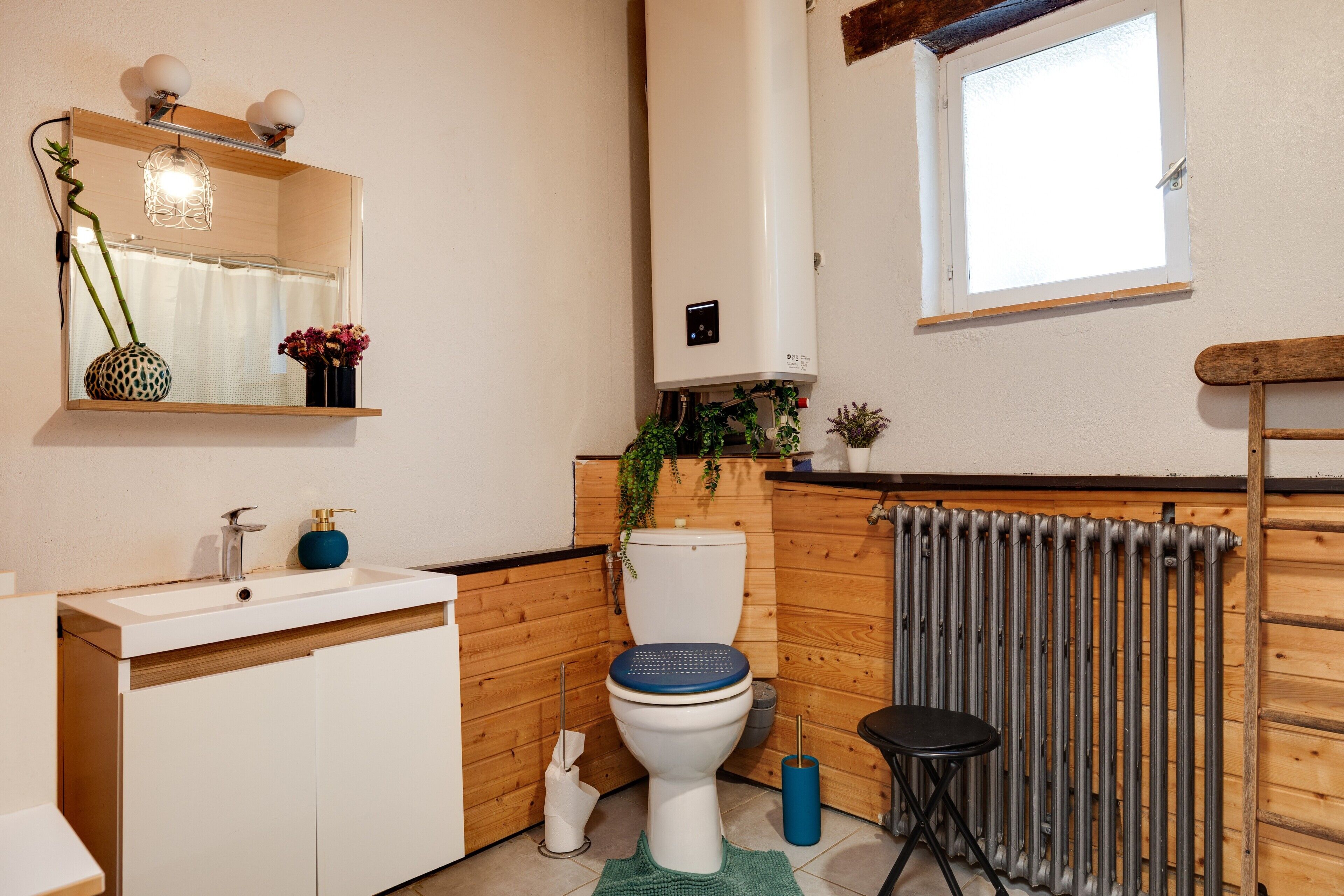A bathroom with a white sink, a toilet, a mirror, a radiator, and a window.