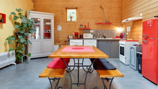 A wooden-paneled kitchen with a table, benches, a refrigerator, and a microwave. - Le Fil Rouge – A Warm Holiday Home Blending Stone and Design in the Countryside (Saint-Pierre-d'Aurillac)