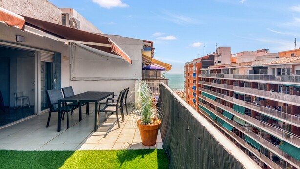 A balcony with a table and chairs, a potted plant, and a view of the sea and buildings. - Apartment 'De Playa En Cullera' with Sea Views, Wi-Fi and Air Conditioning (Cullera)
