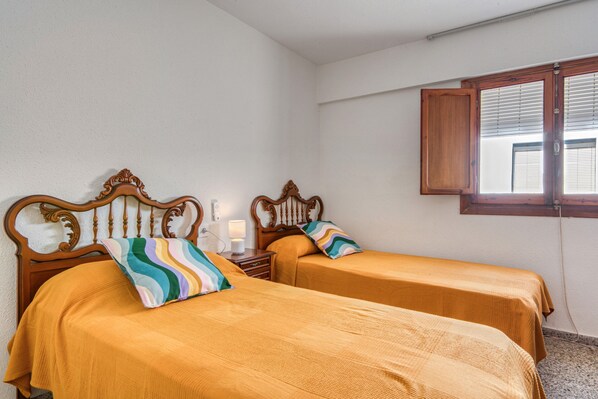 Una habitación con dos camas, cada una con cabecero de madera y almohada a rayas. Entre las camas hay una mesita de noche con una lámpara.
