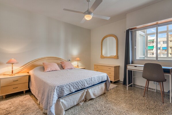 A bedroom with a bed, bedside tables, a desk, a chair, a ceiling fan, and a window.