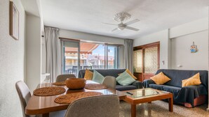 A living room with a sofa, coffee table, and dining table with placemats. - Apartment 'De Playa En Cullera' with Sea Views, Wi-Fi and Air Conditioning (Cullera)