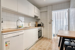 Una cocina con armarios blancos, lavavajillas, horno, microondas y una mesa de madera con sillas.