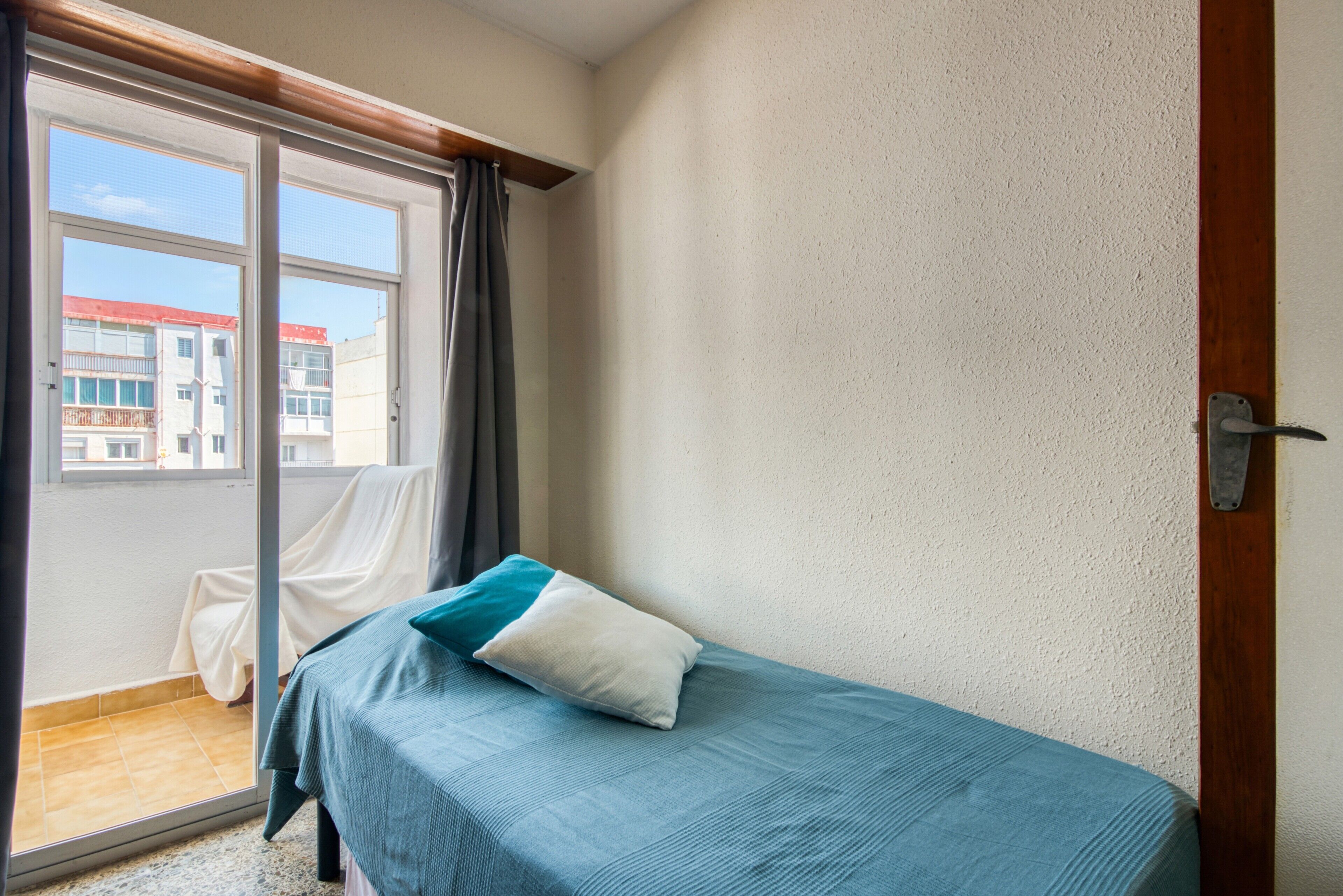 Een kamer met een bed, een raam en uitzicht op gebouwen.