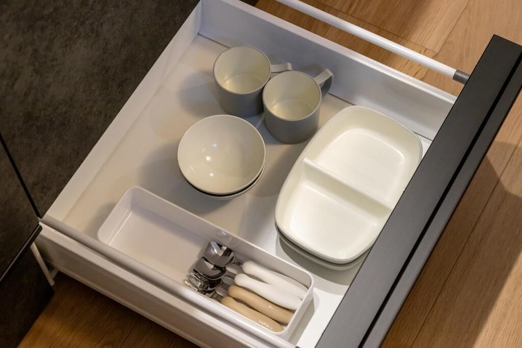 A neatly organized drawer with a set of utensils, three cups, and a plate.
