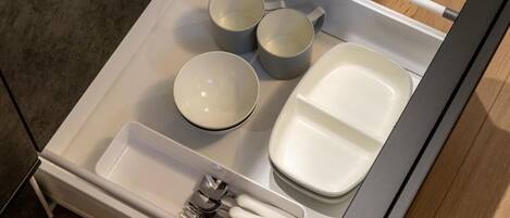A neatly organized drawer with a set of utensils, three cups, and a plate.