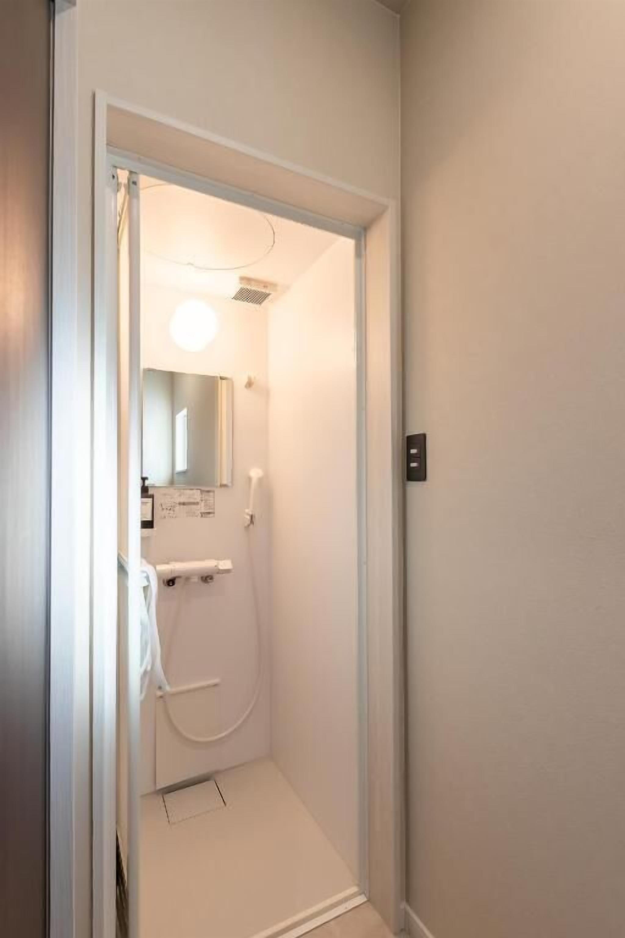 A small, enclosed shower area with a mirror, towel rack, and a light fixture.