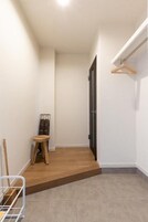 Un pasillo estrecho con suelo de madera, un taburete pequeño, un perchero y una puerta.