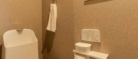 A bathroom with a toilet, a towel rack, a window, and a wall-mounted sink.
