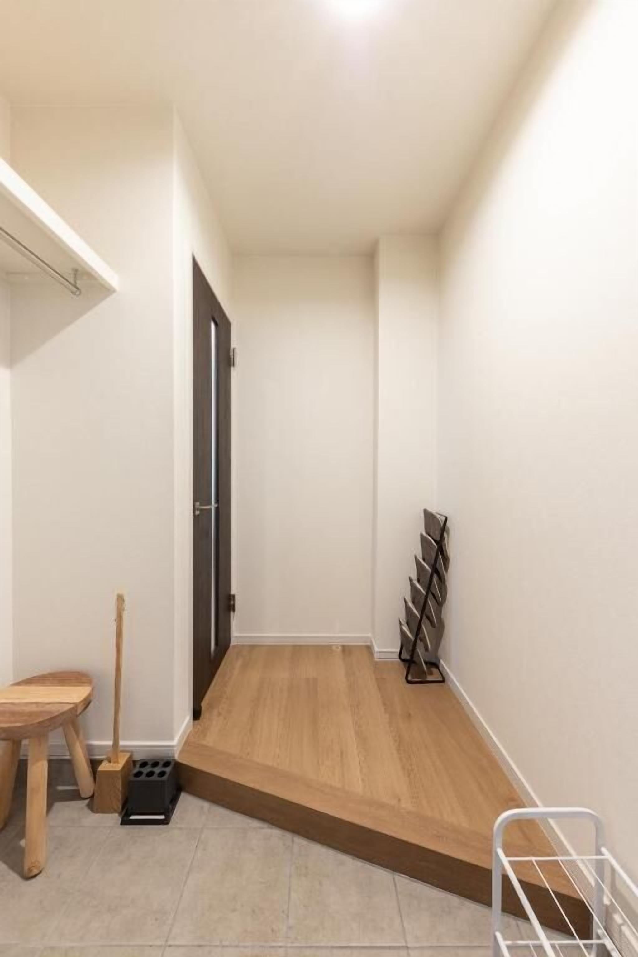 A narrow hallway with a wooden floor, a door on the left, and a metal rack on the right.