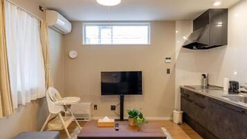 A compact living space with a kitchenette, a television, a dining area, and a window providing natural light.