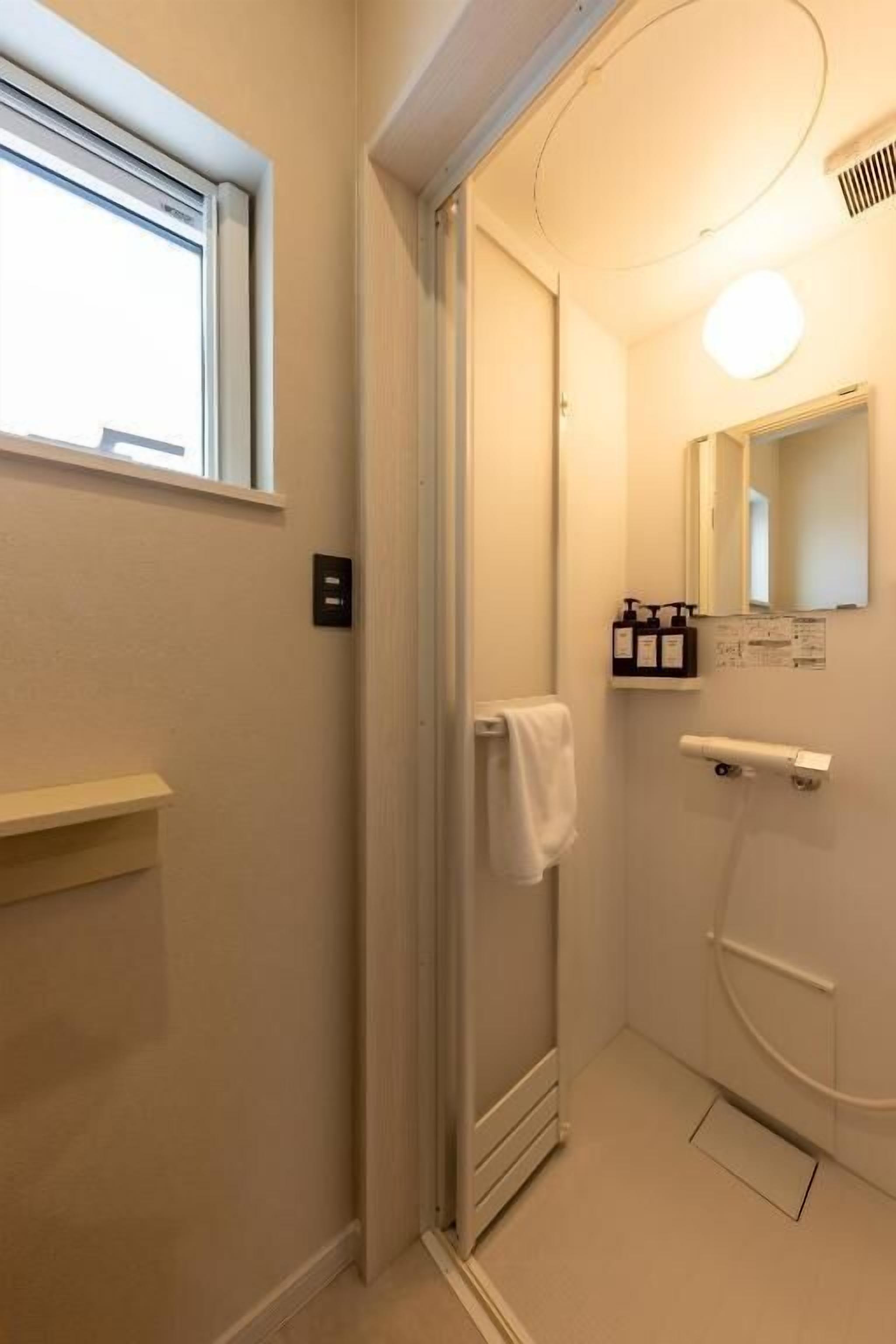 Ett litet, modernt badrum med dusch, handduksställ och ett fönster.