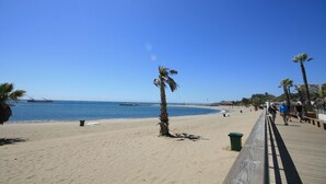 Una playa con un paseo marítimo de madera, palmeras y un cielo azul despejado.