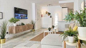 Una sala de estar moderna con un televisor de pantalla plana, una mesa consola de madera y varias plantas en macetas.