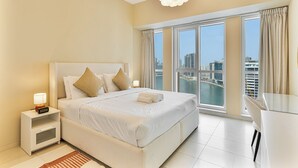A modern hotel room with a large bed, a desk, and a view of the city through floor-to-ceiling windows. - Lush 1BR with Canal View, 9 minutes to Dubai Mall (Dubai)