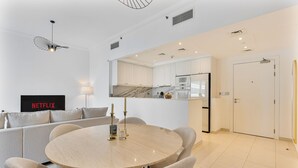 A modern living room with a round wooden table, beige sofas, and a TV displaying 'NETFLIX'. - Lush 1BR with Canal View, 9 minutes to Dubai Mall (Dubai)
