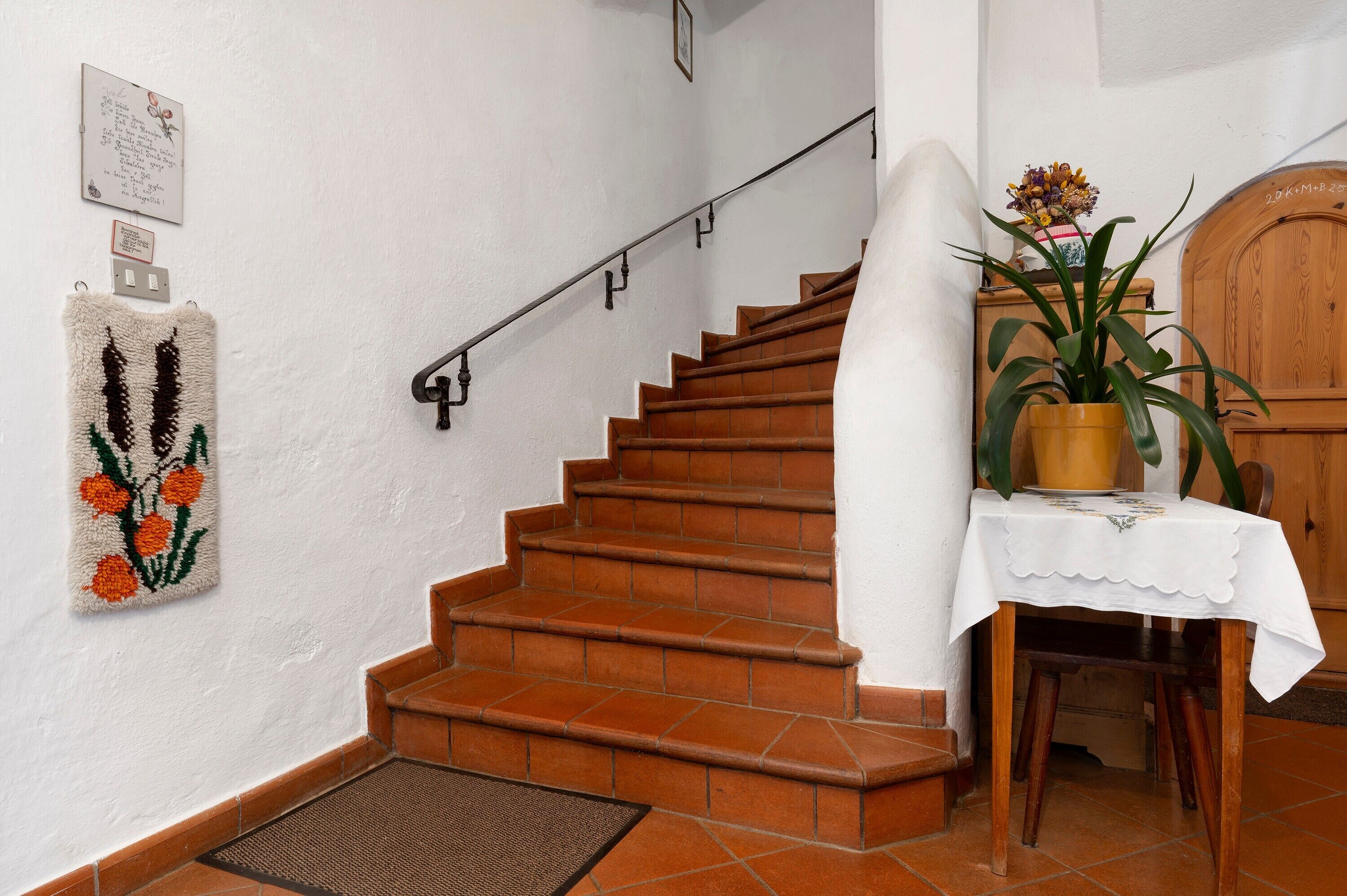 Un escalier avec une rampe, un objet décoratif fixé au mur, une plante en pot et une porte en bois.
