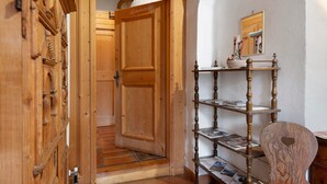A wooden door with intricate carvings, a wooden staircase, and a wooden shelf with books and decorative items. - Apartment 'Helmsdorf Ritterturm' with Mountain View, Shared Garden and Wi-Fi (Lana)