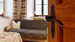 A wooden door with a metal handle, a grey sofa with cushions, and a window with curtains in the background. - Apartment 'Helmsdorf Ritterturm' with Mountain View, Shared Garden and Wi-Fi (Lana)
