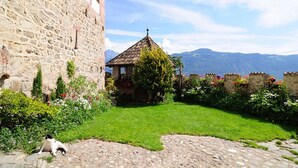 A stone building with a garden, a small gazebo, and a view of mountains.