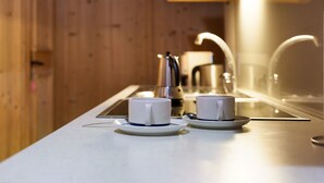 A modern kitchen with two white cups on a white countertop, a kettle, and a sink.