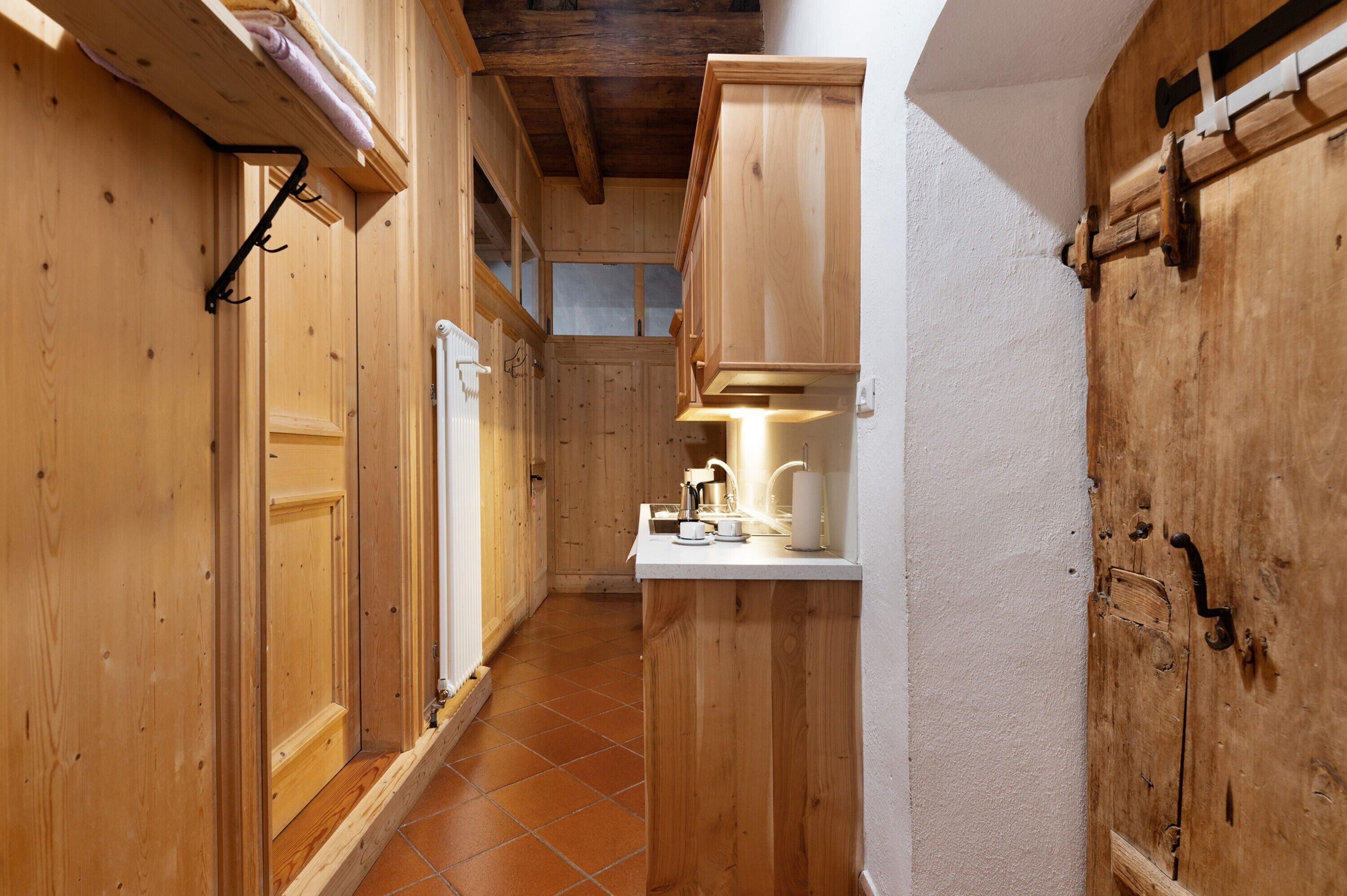 A narrow wooden hallway with a white countertop and a sink, wooden cabinets, and a window.