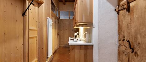 A narrow wooden hallway with a white countertop and a sink, wooden cabinets, and a window.